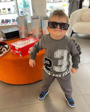 一個幼兒戴著超大太陽眼鏡和運動服在運動鞋店裡擺姿勢。