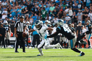 NFL四分衛在日間比賽中躲避防守球員，背景有觀眾。