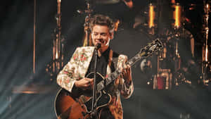 Harry Styles 在現場音樂會表演中於舞台上彈結他。