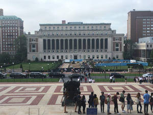 學生們聚集在帶有柱廊的大型大學建築前的圖案廣場上。
