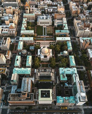 俯瞰一個大學校園，擁有圓頂建築和綠色草坪，周圍環繞著城市摩天大樓。 — 建築 壁紙