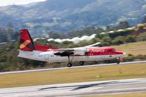 Avianca 飛機從跑道起飛，後面有綠色山丘和建築物。