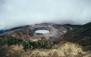 火山口湖被霧氣和崎嶇地形環繞，有綠色植被。