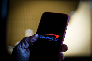 手拿著顯示Capital One標誌的電話，在昏暗的溫暖光線中。
