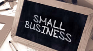 黑板，上面用白色粉筆寫著small business，放在有辦公用品的桌子上。