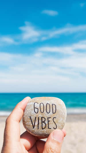 手在沙灘上拿著一塊寫有 good vibes 的石頭。