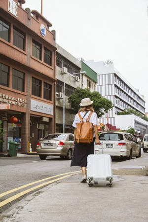 一個戴著帽子和背包的人，拖著行李箱穿過城市街道。