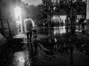 夜晚在淹水的城市街道上推單車的人，帶有反射。 — 雨天 壁紙
