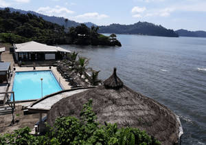 熱帶度假村泳池和茅草屋頂小屋，俯瞰著平靜的海灣和綠色山丘。