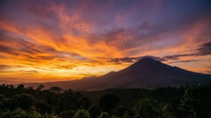 日落時分的火山，叢林上空有鮮豔的橙色和紫色天空
