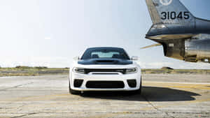 白色Dodge Challenger SRT Hellcat停泊在機場的軍用噴射機旁邊。