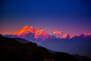 白雪覆蓋的山脈沐浴在橙色夕陽光中，位於黑暗森林山丘之上。