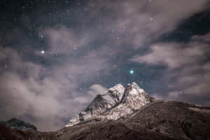 白雪覆蓋的山峰，繁星點點的夜空下，飄動的雲朵和一顆可見的彗星。
