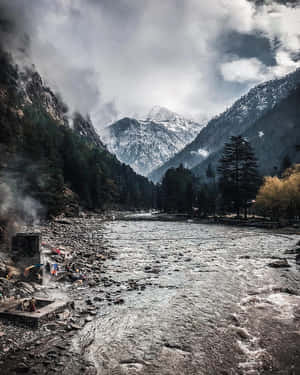 一條河流蜿蜒穿過積雪的山谷，有常綠樹木和霧氣。