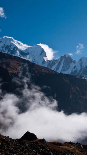 一個人在山頂上，下方有白雪覆蓋的山峰和雲朵。