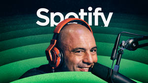 戴著橙色耳機的男子對著麥克風說話，身後有Spotify標誌。