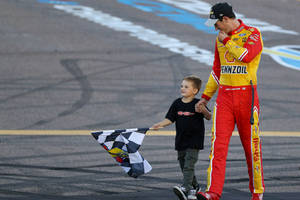 NASCAR車手與手持格仔旗的小男孩在賽道上。