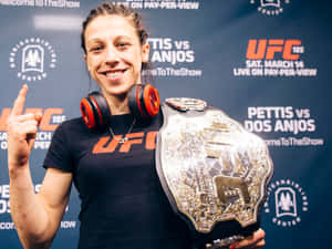 女性UFC拳手戴著耳機，手持冠軍腰帶並向上指。
