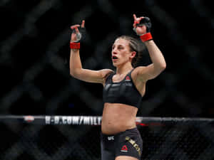 女性MMA拳手在八角籠中高舉雙臂慶祝勝利。