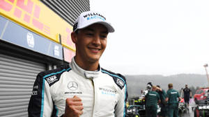 身穿威廉姆斯車隊賽車服的F1車手在賽道車庫微笑並揮拳。