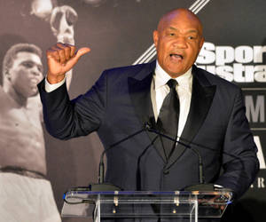 一個穿西裝的男子在講台上演講，身後有拳擊海報。 — 拳擊 壁紙