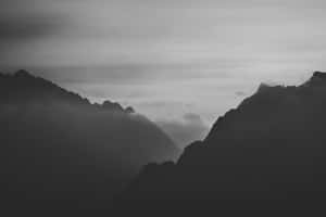 剪影般的山峰在霧氣雲層中升起，形成單色景觀。 — MacBook Pro 壁紙