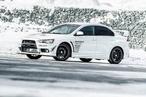 白色三菱Lancer Evolution X在雪路上靠近石牆飄移。