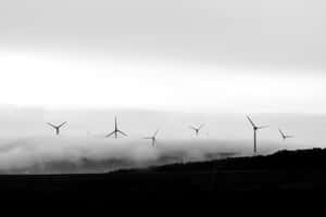 在寧靜的黑白風景中，風力發電機高高聳立在霧氣籠罩的山谷之上。 — 黎明 壁紙