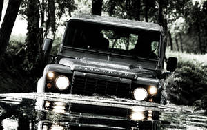 黃昏時分，一輛 Land Rover Defender 涉水穿過森林溪流。