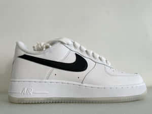 純色背景上帶有黑色Swoosh的白色Nike Air Force 1運動鞋。