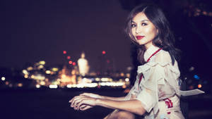 身穿白色連衣裙的女性在夜晚坐在水邊，身後有城市燈光。 — 星空夜 壁紙