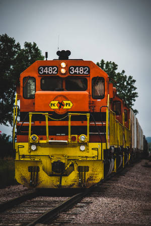 橙色和黃色的貨運火車引擎在鐵路軌道上，後面有樹木。