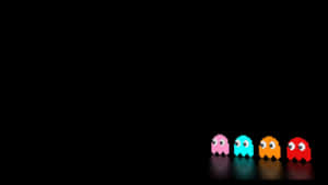 四個經典 Pac-Man 鬼魂，分別為粉紅色、青色、橙色和紅色，在深色表面上排成一排。 — 可愛動漫女仔 壁紙