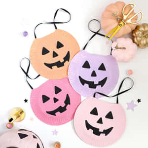 粉彩色紙碟萬聖節面具，帶有黑色鏤空，周圍環繞著裝飾性南瓜和手工工具。 — 萬聖節恐怖 壁紙
