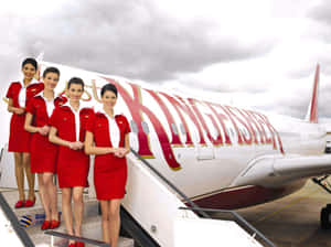四名身穿紅色制服的航空公司員工在飛機樓梯上擺姿勢。 — 夢境 GIF 壁紙