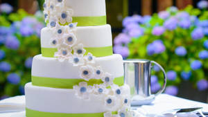 四層白色結婚蛋糕，綠色絲帶和糖花，戶外。