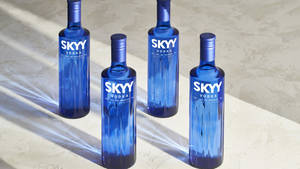 四支藍色SKYY伏特加酒瓶在明亮的陽光下，置於紋理表面上。