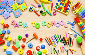 色彩繽紛的學校用品和玩具排列在木質表面上，拼出 back to school。