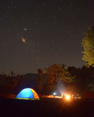 露營者在繁星點點的夜空下，圍坐在營火旁，附近有一個發光的帳篷。