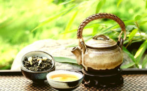 陶瓷茶壺和茶杯與茶葉在編織墊上，靠近竹子。