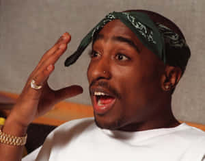 Tupac Shakur 身穿白襯衫，戴著綠色頭巾和金飾，做出驚訝的表情。