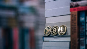 三枚金色加密貨幣硬幣放在一堆書上。 — 加密貨幣 壁紙