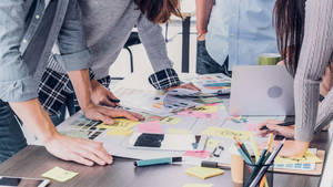 Design team brainstorming with sticky notes and laptops on a wooden desk.