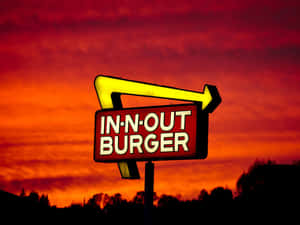 一個明亮的黃色箭頭標誌，代表 In-N-Out Burger，映襯著充滿活力的日落天空。