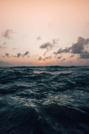 日落時分的海浪，粉紅和橙色天空，散落的雲朵。