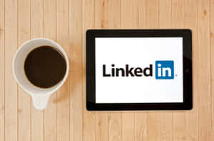平板電腦顯示LinkedIn標誌，旁邊有咖啡杯在木桌上。