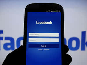 手拿著手機顯示Facebook登入畫面，背景有模糊標誌。