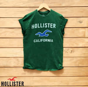 綠色Hollister California T恤掛在木衣架上，背景為木牆。