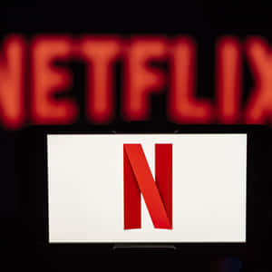 智能手機顯示 Netflix 標誌，背景有模糊的 Netflix 標牌。
