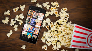 智能手機顯示Netflix電影，周圍散落爆谷在木頭上。